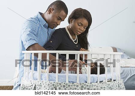 Stock Photography - Couple admiring sleeping baby son in crib. Fotosearch
