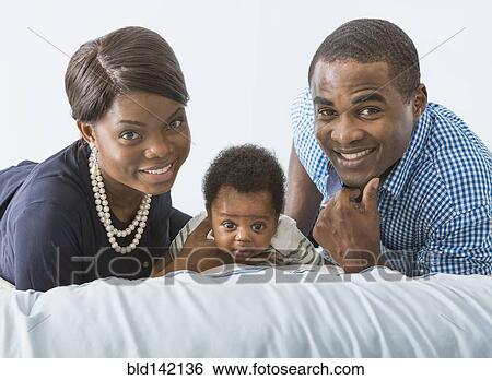 Stock Photograph - Couple smiling with baby son on bed. Fotosearch