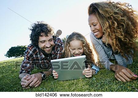 Stock Photograph - Family using digital tablet in grassy field. Fotosearch