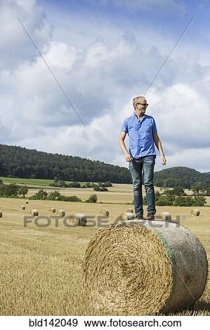 Farmer standing on hay bale in field View Large Photo Image Stock Photo - Farmer standing on hay bale in field. Fotosearch