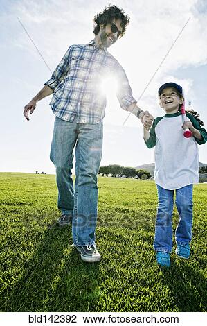 Stock Image - Father and daughter walking in grassy field. Fotosearch