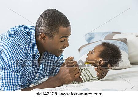 Stock Photo - Father cradling baby son on bed. Fotosearch