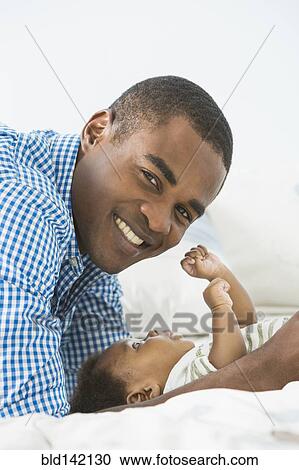 Father smiling with baby son on bed View Large Photo Image Stock Image - Father smiling with baby son on bed. Fotosearch