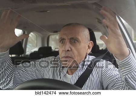 Picture - Frustrated Hispanic senior man driving car in traffic. Fotosearch
