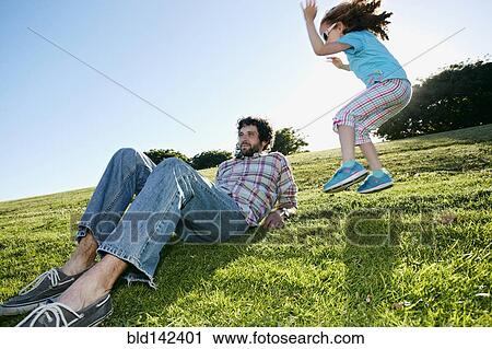 Stock Image - Girl jumping near father in grassy field. Fotosearch