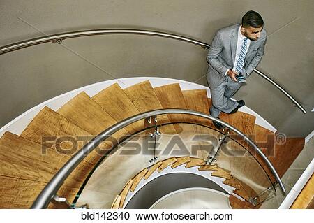 Stock Image - High angle view of Middle Eastern businessman standing on spiral staircase. Fotosearch