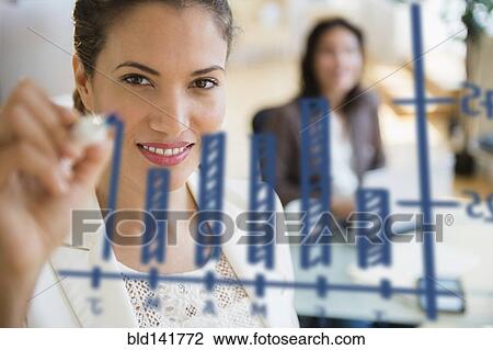 Stock Image - Hispanic businesswoman drawing chart on glass in office. Fotosearch