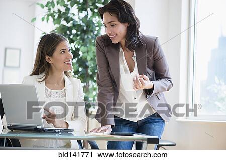 Stock Image - Hispanic businesswomen working together in office. Fotosearch