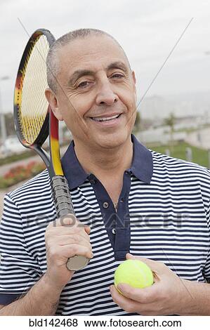 Stock Photo - Hispanic senior man carrying tennis racket and ball. Fotosearch