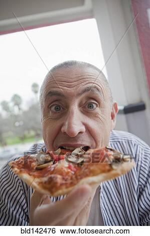 Stock Photograph - Hispanic senior man eating slice of pizza. Fotosearch