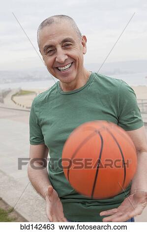 Stock Image - Hispanic senior man playing basketball outdoors. Fotosearch