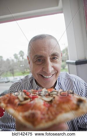 Stock Photography - Hispanic senior man sharing slice of pizza. Fotosearch