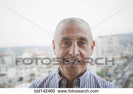 Stock Image - Hispanic senior man smiling near scenic view of cityscape. Fotosearch