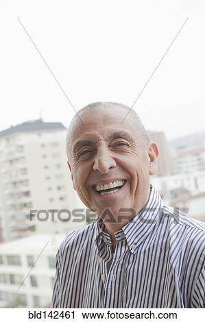 Stock Image - Hispanic senior man smiling near scenic view of cityscape. Fotosearch