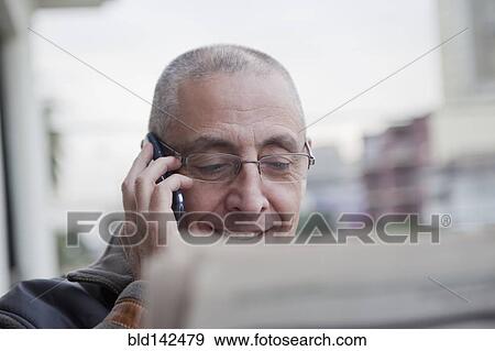Stock Photo - Hispanic senior man talking on cell phone and reading newspaper. Fotosearch