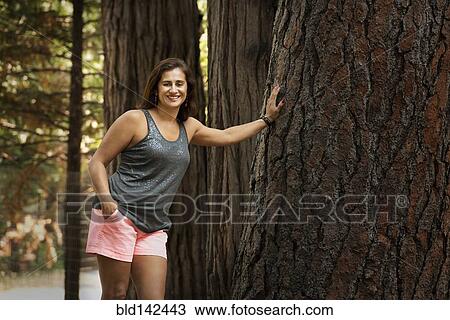 Stock Image - Hispanic woman leaning on enormous tree. Fotosearch
