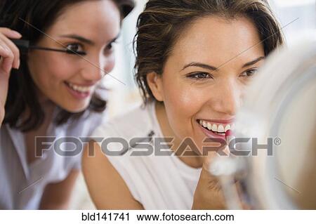 Stock Image - Hispanic women applying makeup in mirror. Fotosearch