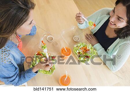 Stock Image - Hispanic women eating salad together at table. Fotosearch