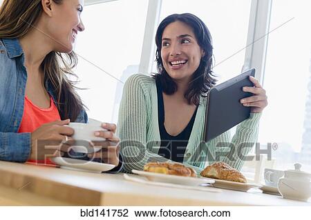 Stock Image - Hispanic women using digital tablet at breakfast. Fotosearch