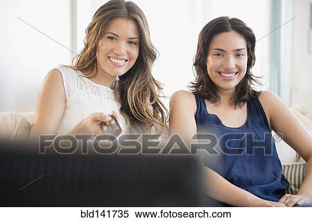 Stock Photography - Hispanic women watching television on sofa. Fotosearch