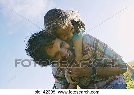 Stock Photography - Low angle view of father carrying daughter piggyback outdoors. Fotosearch