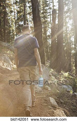 Stock Image - Man hiking on dirt trail in forest. Fotosearch