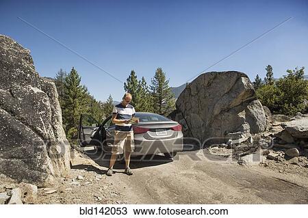 Stock Image - Man reading near car on dirt road. Fotosearch