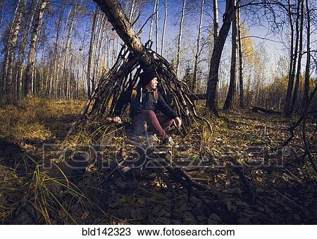 Stock Image - Man sitting in wooden shelter in forest. Fotosearch