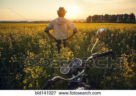Stock Photo - Mari man standing near motorcycle in field of flowers. Fotosearch