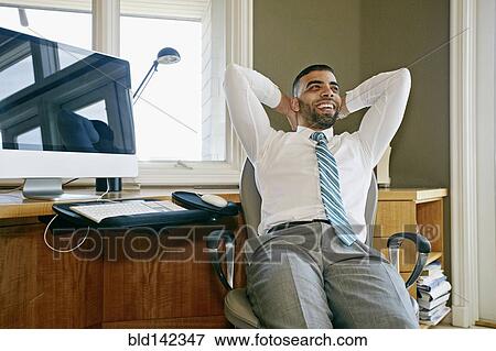 Stock Photo - Middle Eastern businessman relaxing in chair at desk in office. Fotosearch
