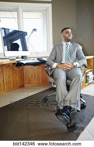 Stock Photograph - Middle Eastern businessman relaxing in chair at desk in office. Fotosearch