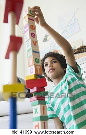 Stock Photo - Mixed race boy building wooden block tower in living room. Fotosearch