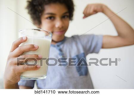 Stock Image - Mixed race boy flexing his muscle and drinking glass of milk. Fotosearch