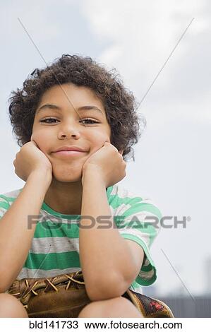 Stock Image - Mixed race boy holding baseball glove outdoors. Fotosearch