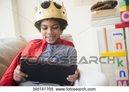 Stock Photography - Mixed race boy in costume using digital tablet in living room. Fotosearch
