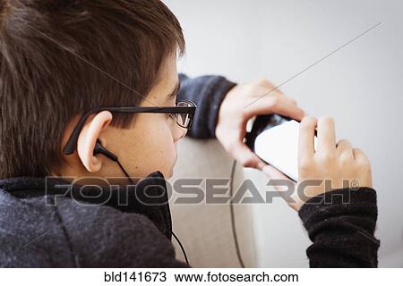 Stock Image - Mixed race boy listening to earbuds and using cell phone. Fotosearch