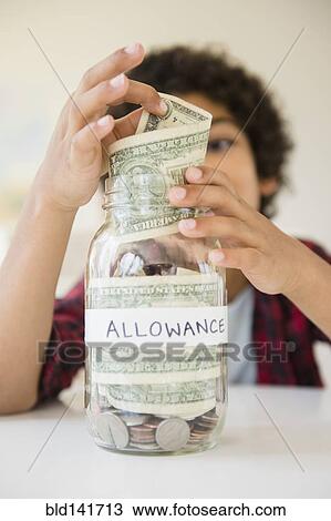 Stock Image - Mixed race boy putting allowance in savings jar. Fotosearch
