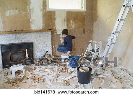 Stock Photo - Mixed race boy stripping wallpaper in living room. Fotosearch