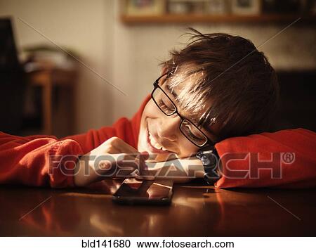 Stock Image - Mixed race boy using cell phone at table. Fotosearch