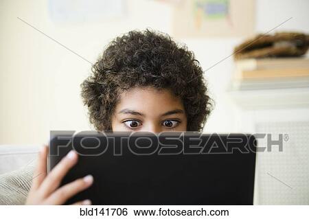 Stock Photograph - Mixed race boy using digital tablet in living room. Fotosearch