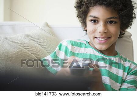 Stock Image - Mixed race boy watching television on sofa. Fotosearch
