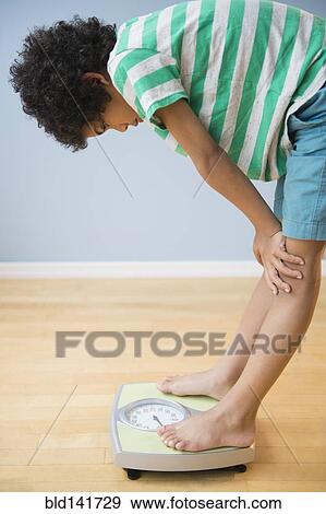 Mixed race boy weighing himself on scale View Large Photo Image Stock Photo - Mixed race boy weighing himself on scale. Fotosearch