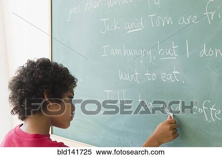 Stock Photography - Mixed race boy writing on chalkboard in grammar lesson. Fotosearch