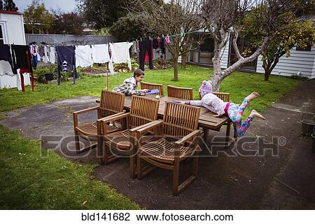 Stock Image - Mixed race brother and sister playing at table in backyard. Fotosearch