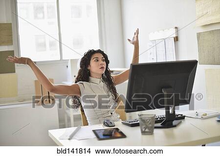 Picture - Mixed race businesswoman frustrated at computer at desk in office. Fotosearch