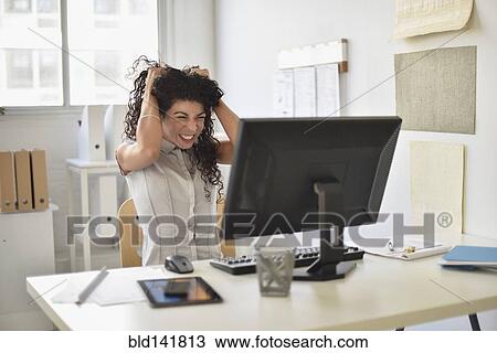 Stock Image - Mixed race businesswoman frustrated at computer at desk in office. Fotosearch
