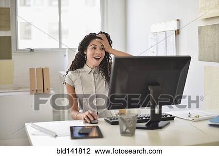 Stock Image - Mixed race businesswoman gasping at computer at desk in office. Fotosearch