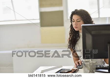 Stock Photography - Mixed race businesswoman using cell phone and computer at desk in office. Fotosearch