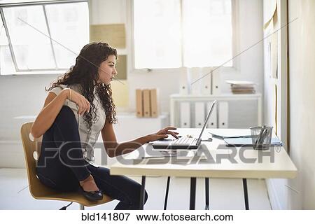 Stock Photo - Mixed race businesswoman working on laptop at desk in office. Fotosearch