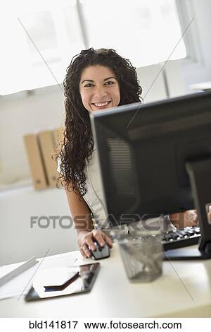 Stock Photo - Mixed race businesswoman working on computer at desk in office. Fotosearch